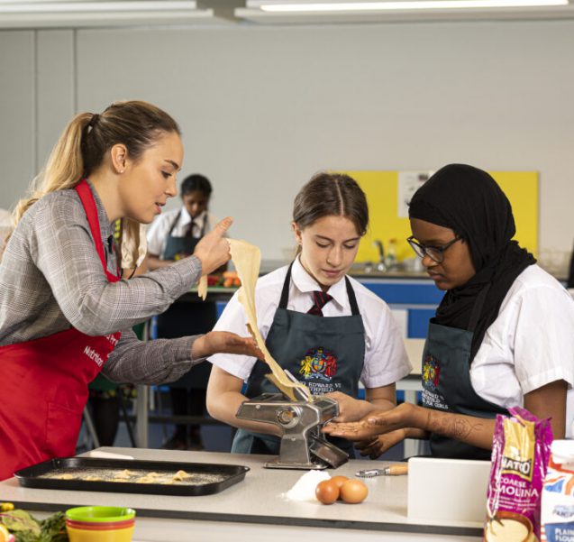 A teacher and students engaging in a cooking class, preparing a meal together in a school kitchen, promoting culinary skills and teamwork.