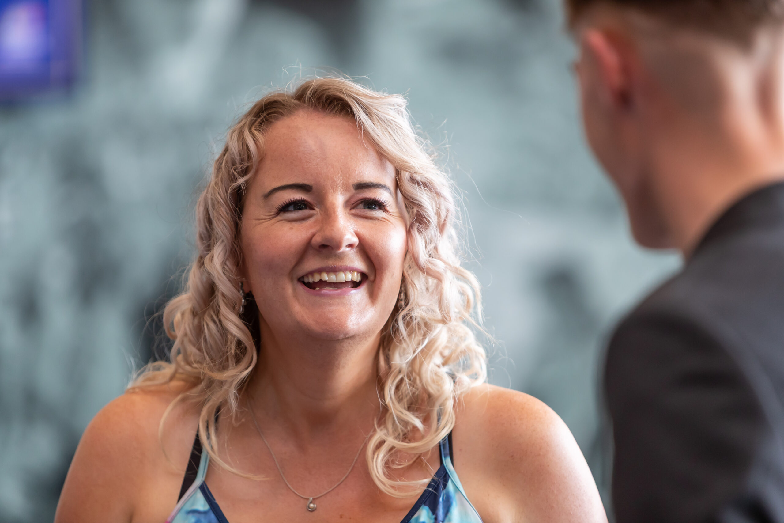 A woman with blonde curly hair smiling while looking at a man in a suit