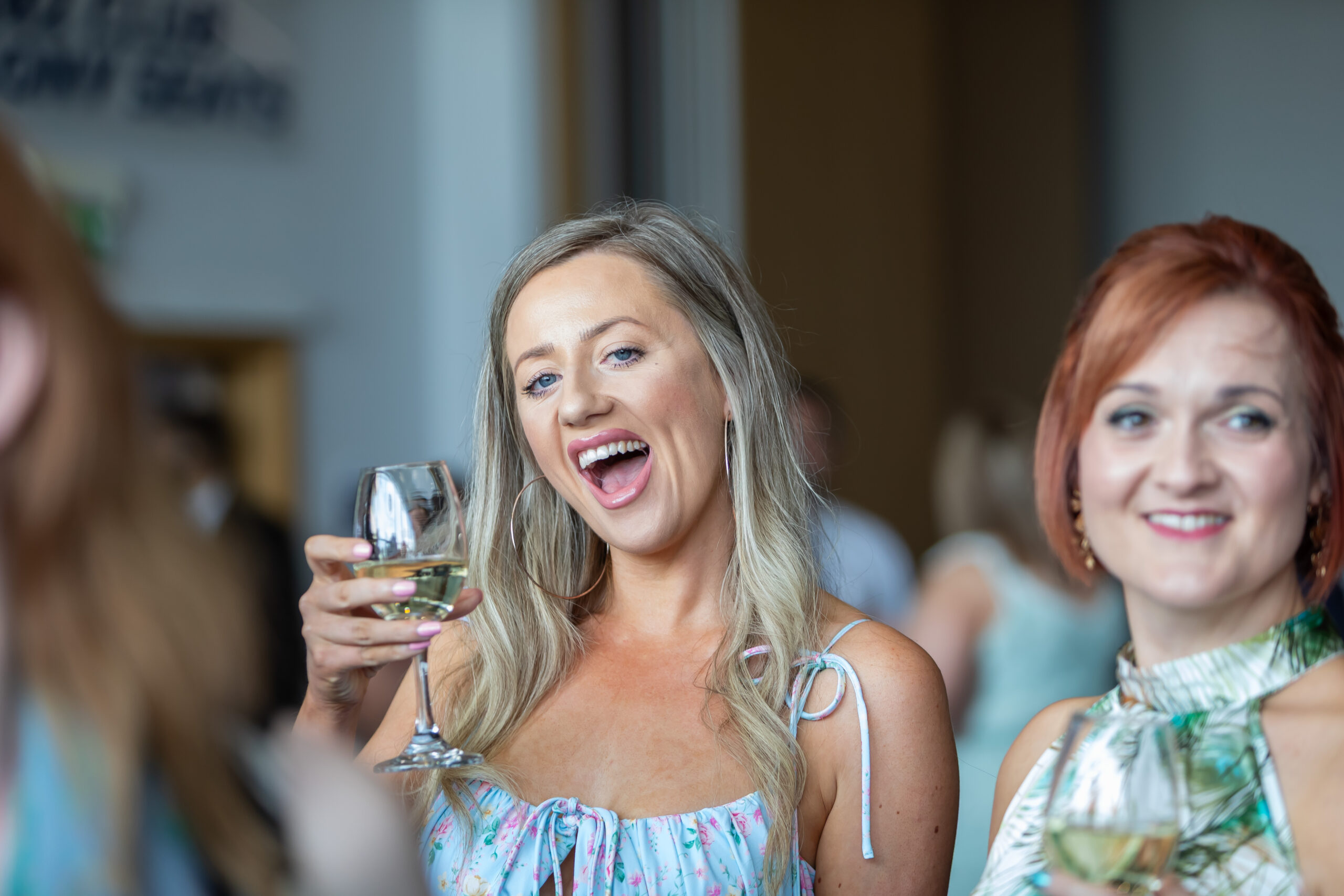 Two women smiling and toasting with glasses of white wine in a social setting