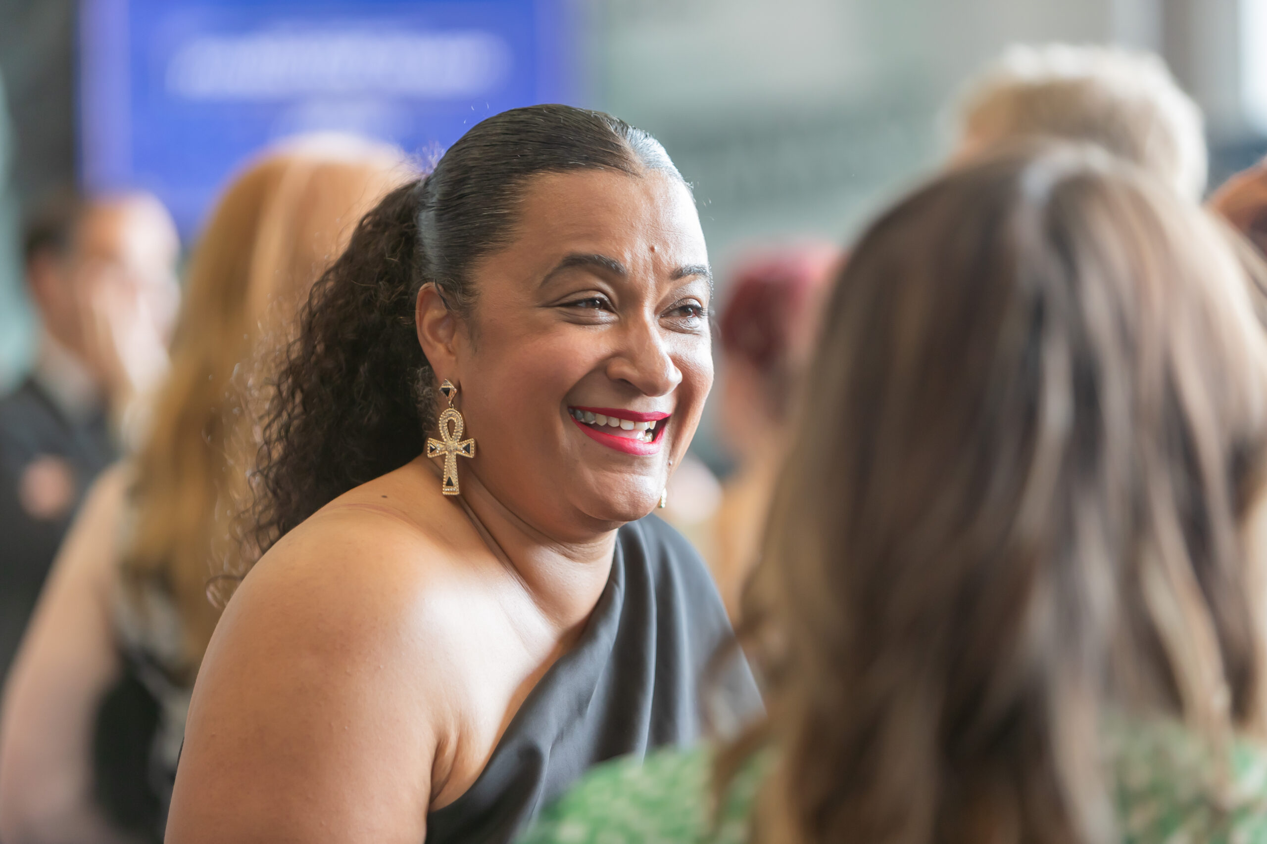 A smiling woman with dark hair and gold earrings at a formal event, engaging with another guest.