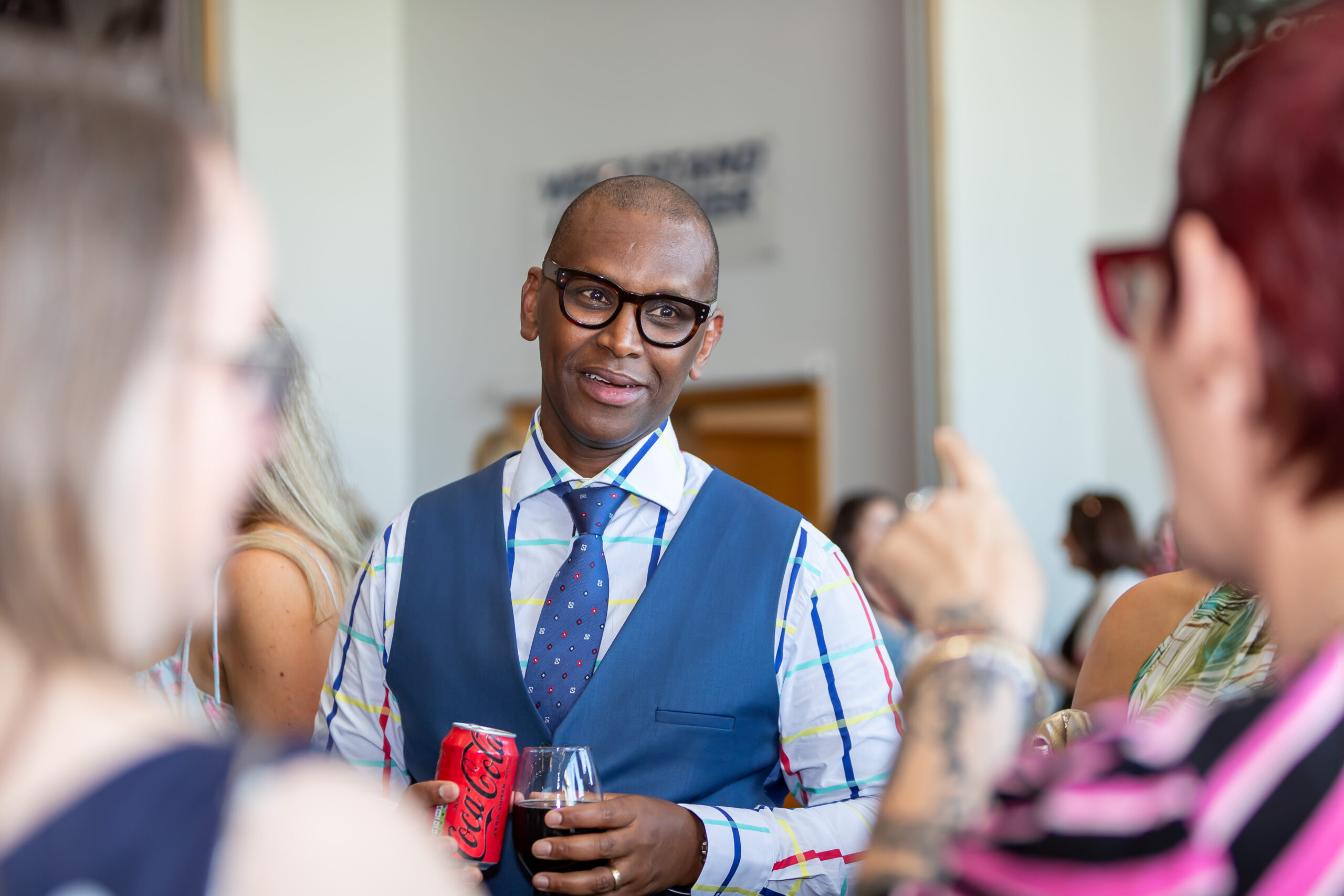 Man in a blue vest and tie standing and talking to two women at a social event.