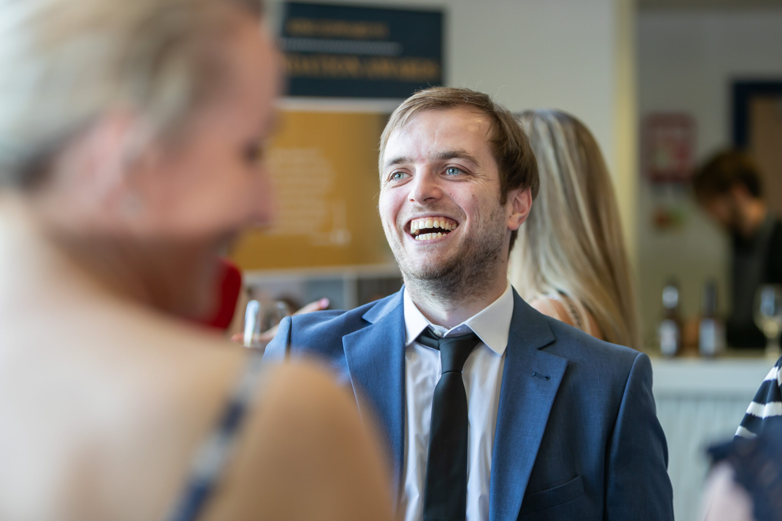 A young man in a blue suit smiling and talking to people at a formal event