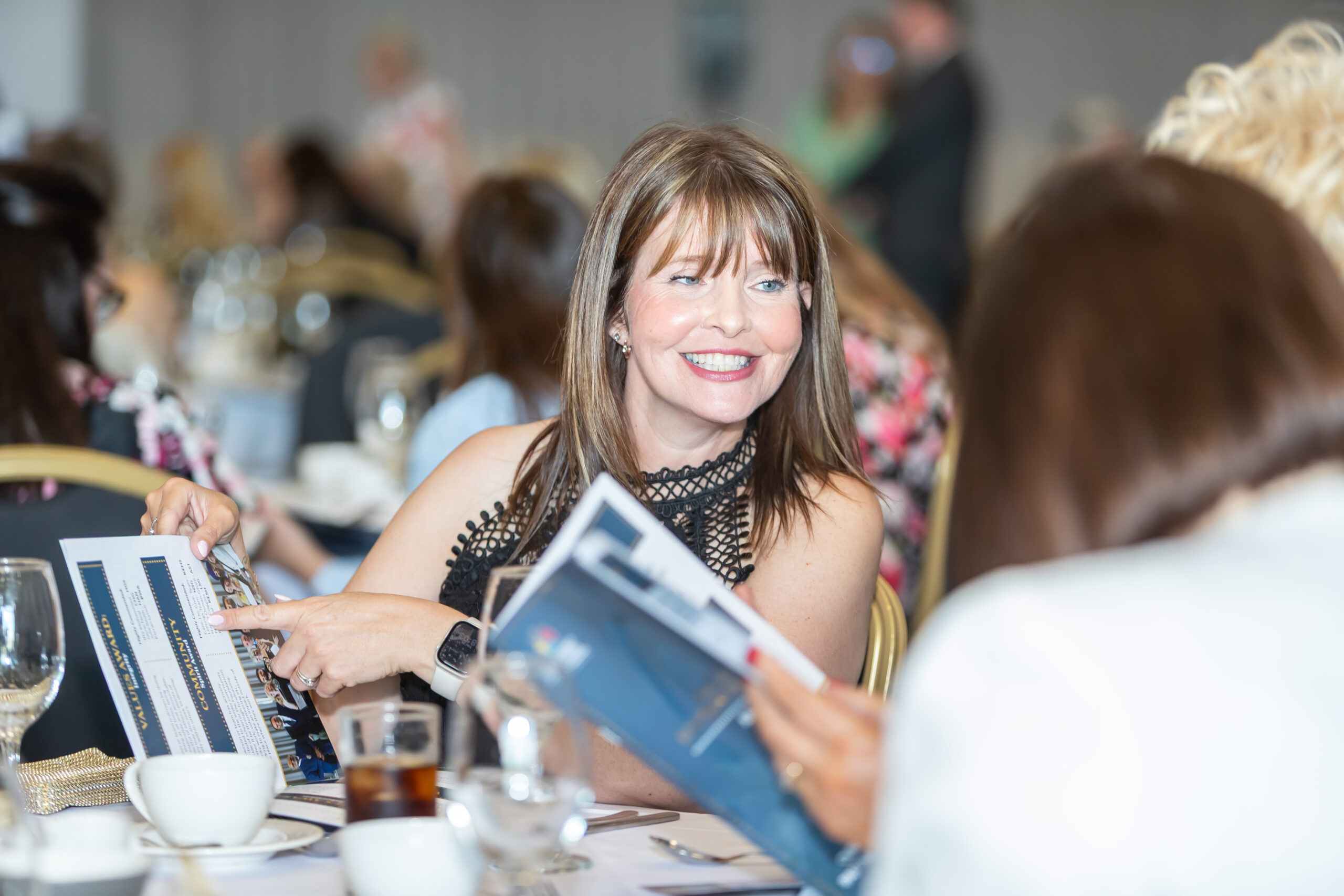 A female student smiling while looking at a menu with another student in a dining setting, likely participating in a school event or educational activity.