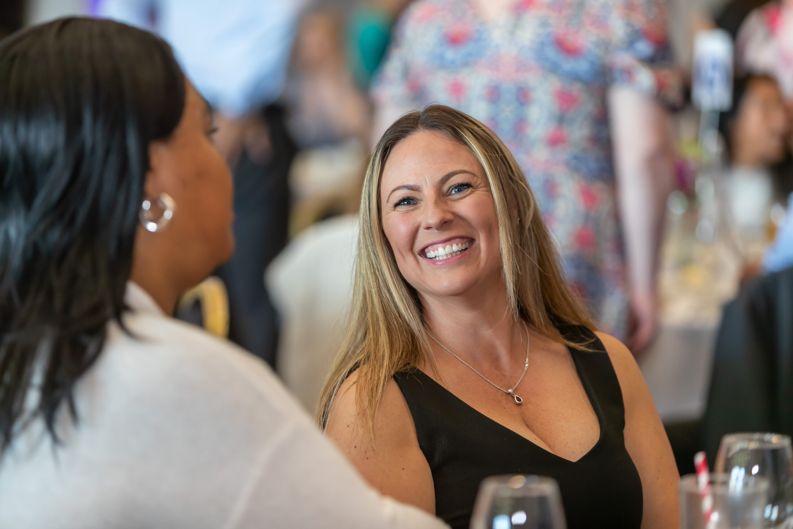 Two women smiling and looking at each other while sitting at a restaurant table, engaged in deep conversation or laughter.