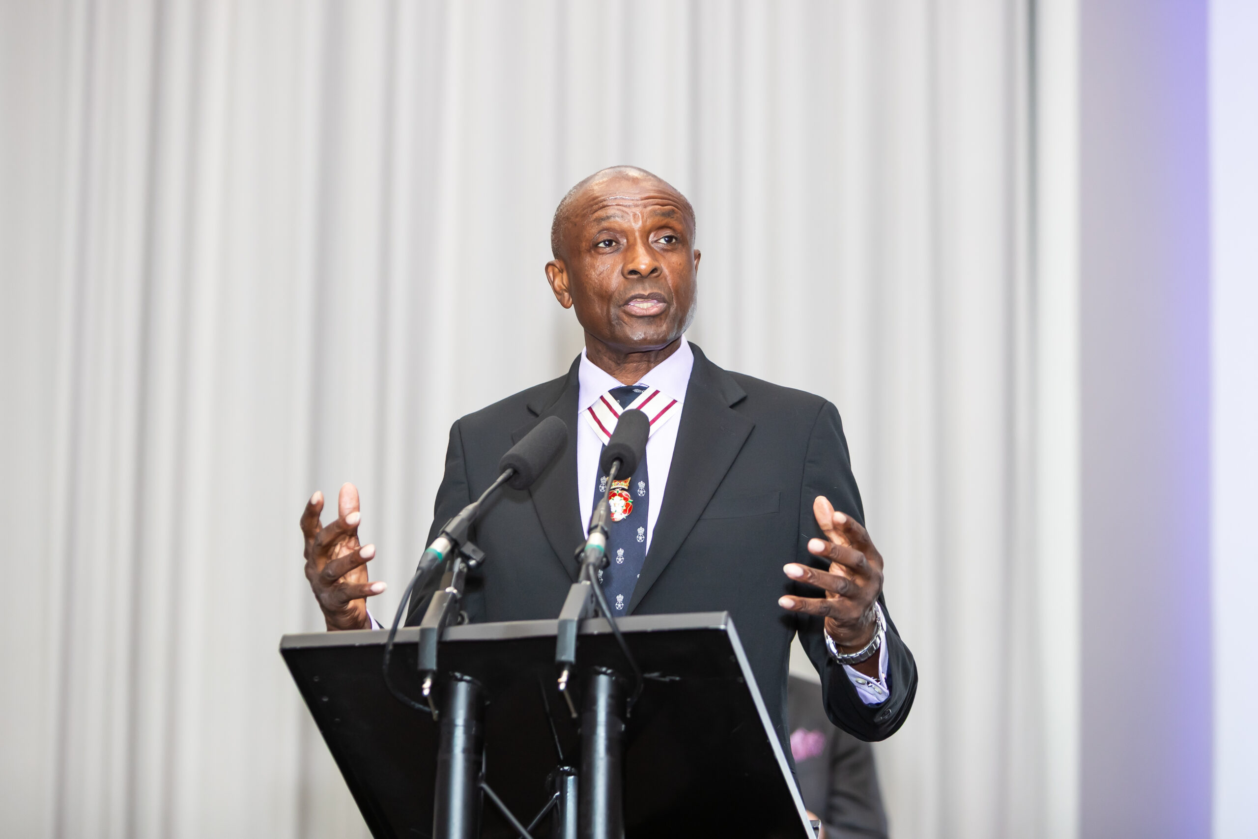 A man in a suit speaking at a lectern with two microphones