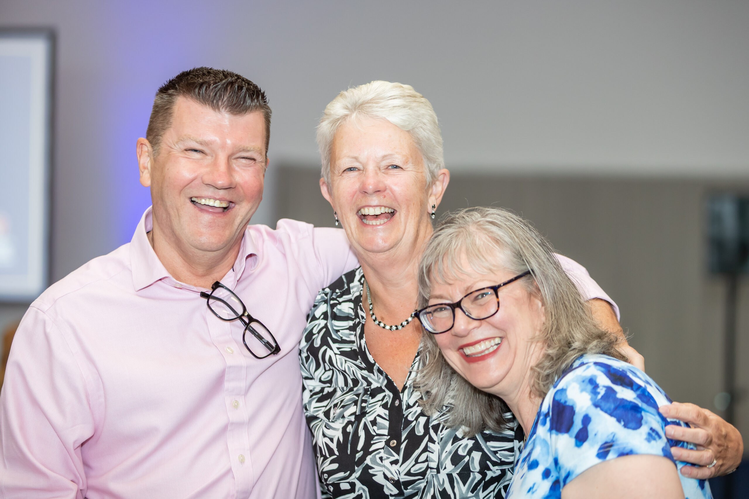 Three smiling adults standing together, arms around each other