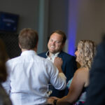 A man smiling while talking to a woman at a social event, surrounded by other people.