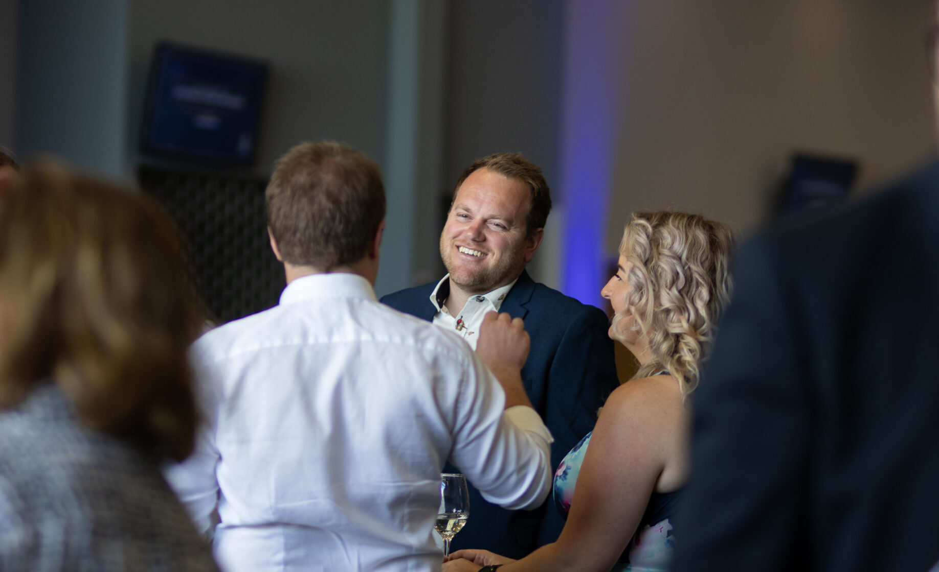 A man smiling while talking to a woman at a social event, surrounded by other people.