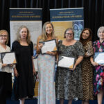 Six women proudly holding certificates on stage at a Kevi Foundation event, celebrating educational achievements.