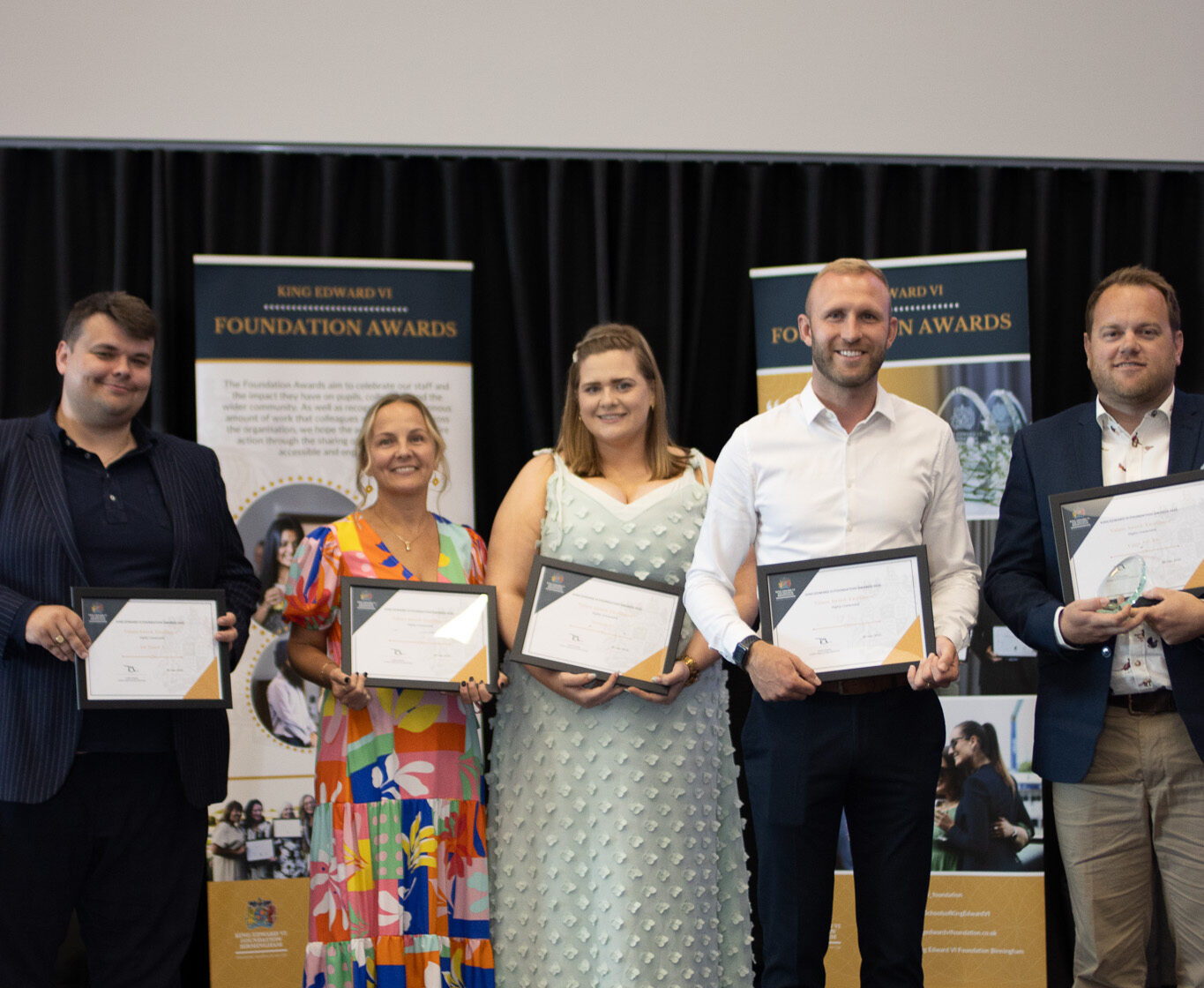Group of students proudly holding certificates in front of banners, celebrating academic achievement and educational milestone.