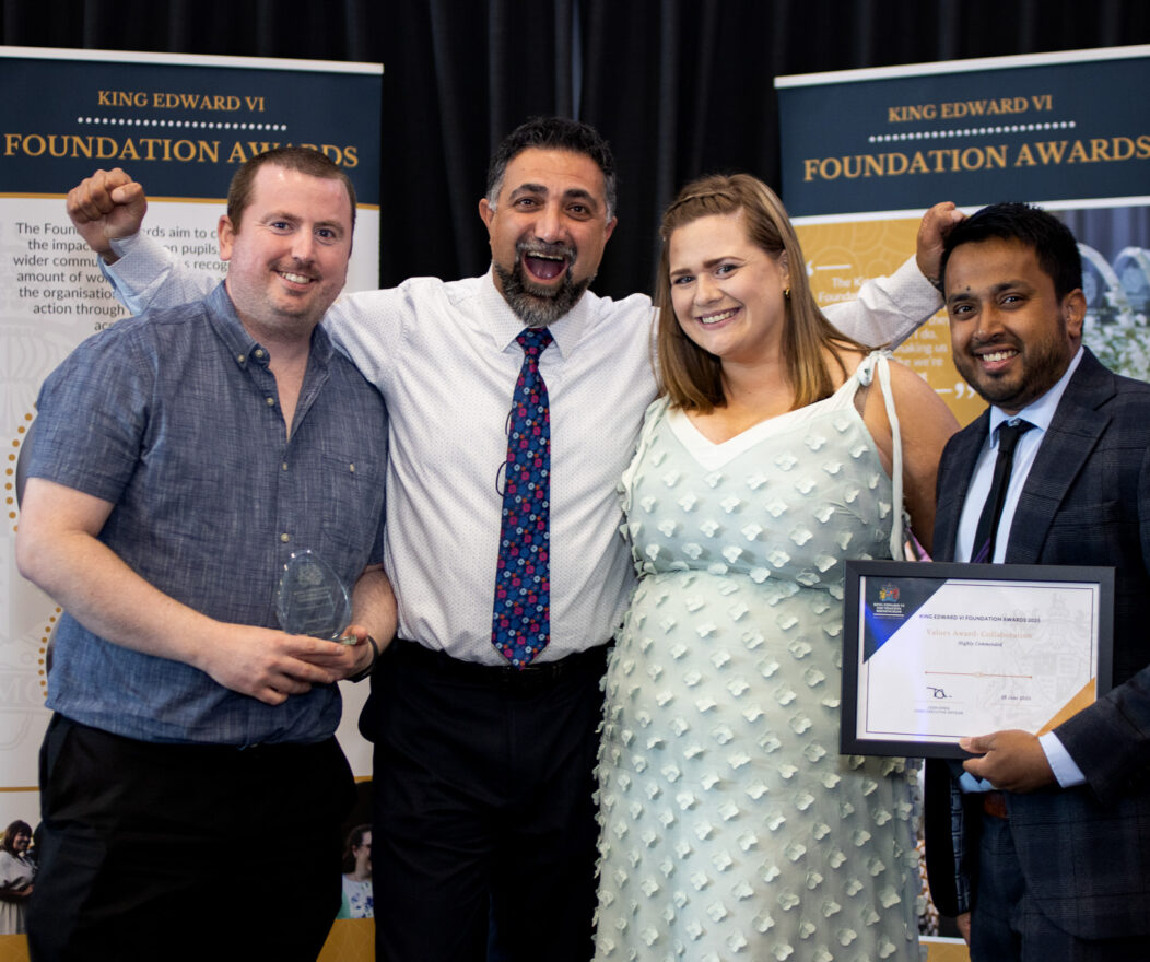 Four people posing for a photo at an awards ceremony, with two of them holding an award and a certificate, smiling and celebrating.