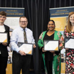 Four individuals proudly holding certificates in a formal setting, likely an award ceremony or recognition event on campus.