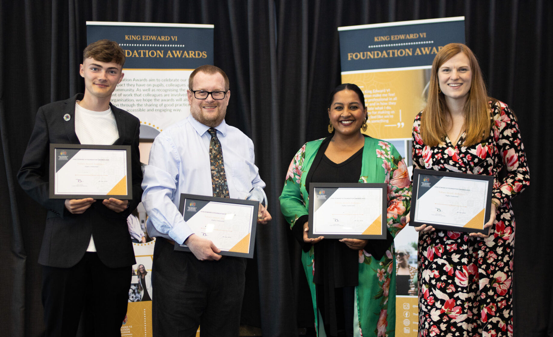 Four individuals proudly holding certificates in a formal setting, likely an award ceremony or recognition event on campus.