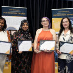 Four women proudly holding certificates in front of a black curtain and Foundation Awards banners, celebrating educational achievements.