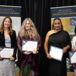 Four women proudly hold certificates on stage at the Kevi Foundation Awards, smiling and posing together in formal attire.
