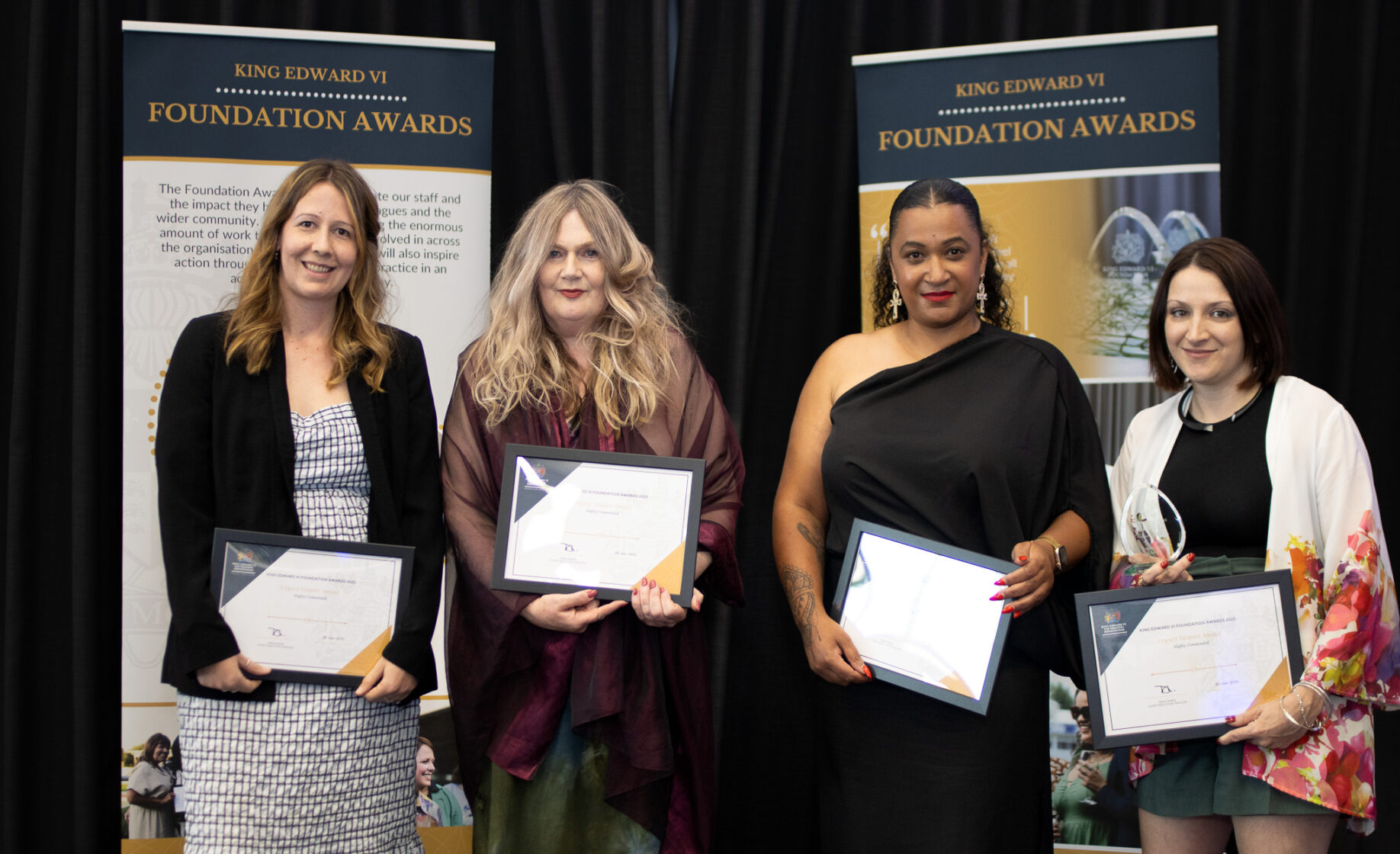 Four women proudly hold certificates on stage at the Kevi Foundation Awards, smiling and posing together in formal attire.