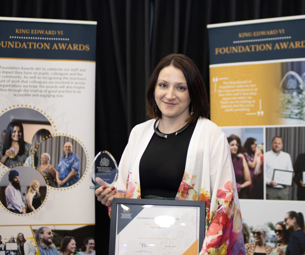A woman proudly holding an award and certificate, standing in front of Foundation Awards banners, celebrating educational achievement.