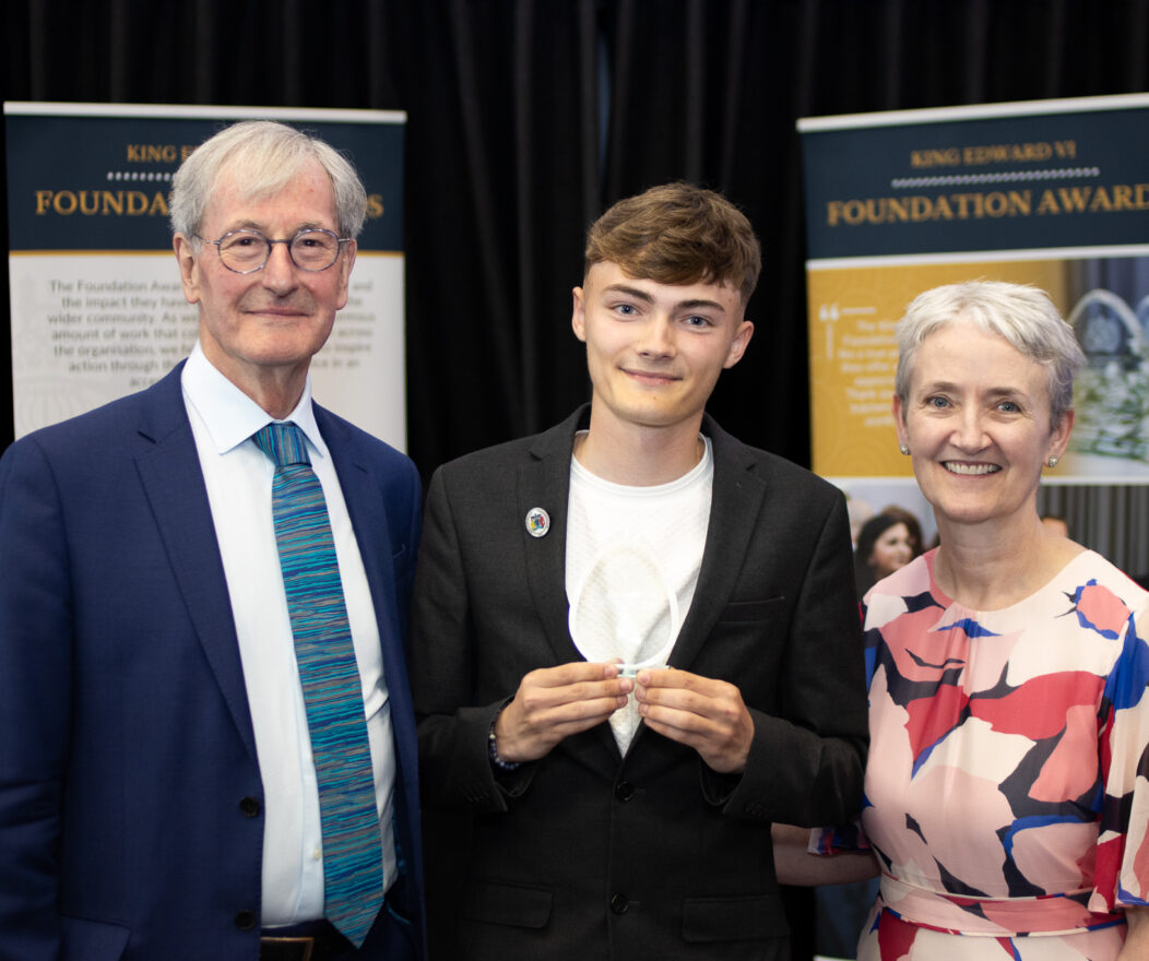 A student proudly holding an award with two adults, likely parents or educators, at the Kevi Foundation Awards, celebrating student achievement.