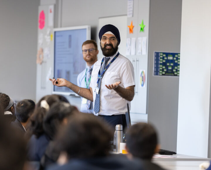 Two male teachers standing at the front of a classroom, engaging with students.